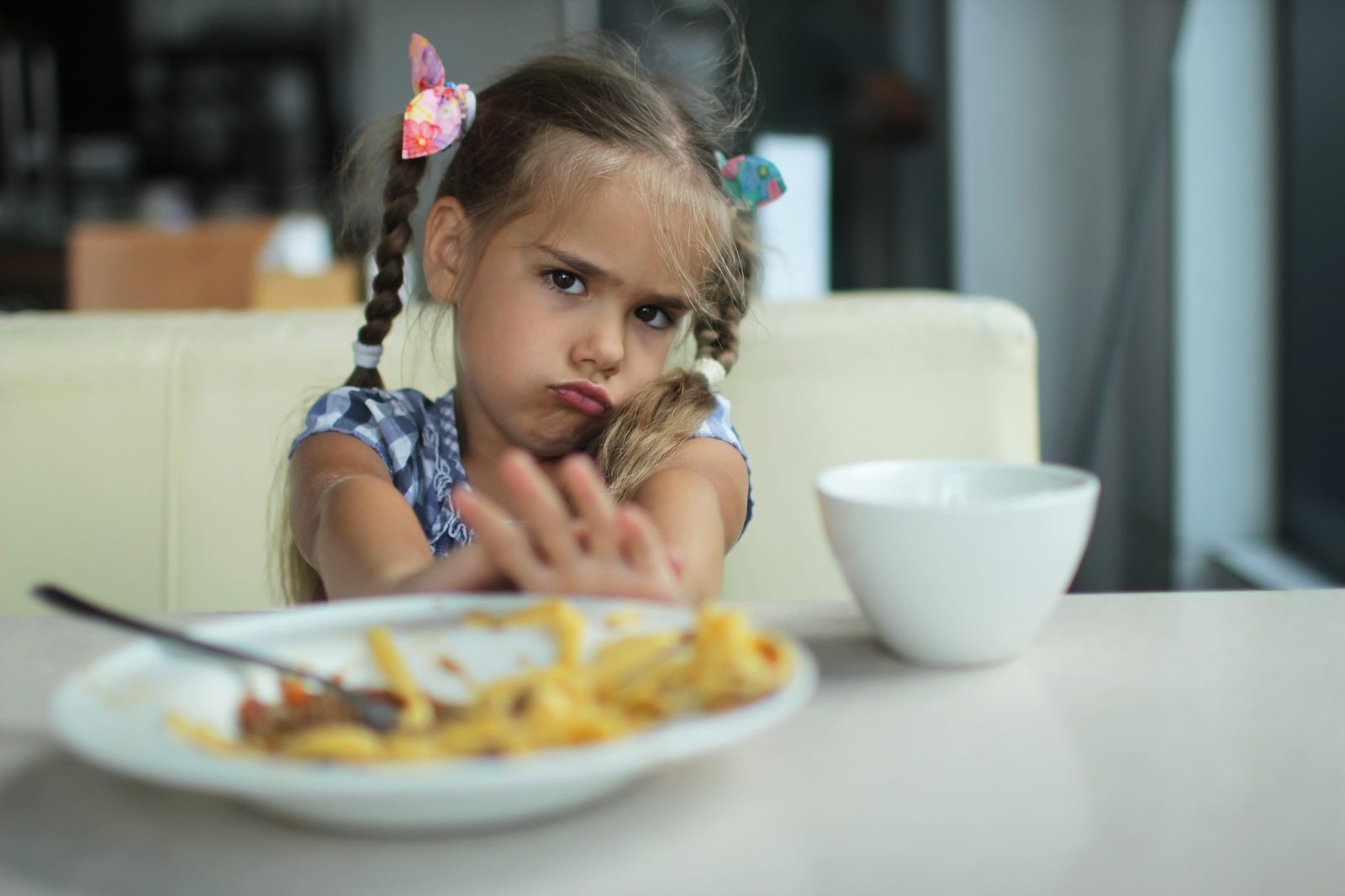 Niña aparta con la mano un plato de comida en la mesa, mostrando rechazo alimentario