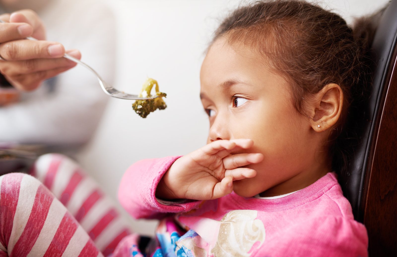 Niña pequeña rechaza una cucharada de brócoli tapándose la boca, un ejemplo de las dificultades alimentarias del ARFID en niños